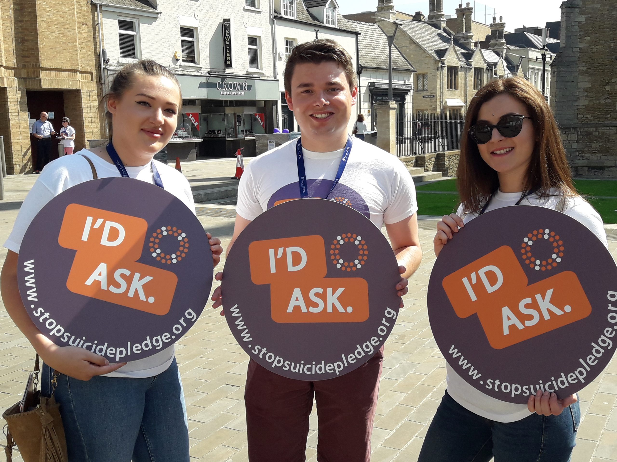 Three people holding the I'd Ask sign
